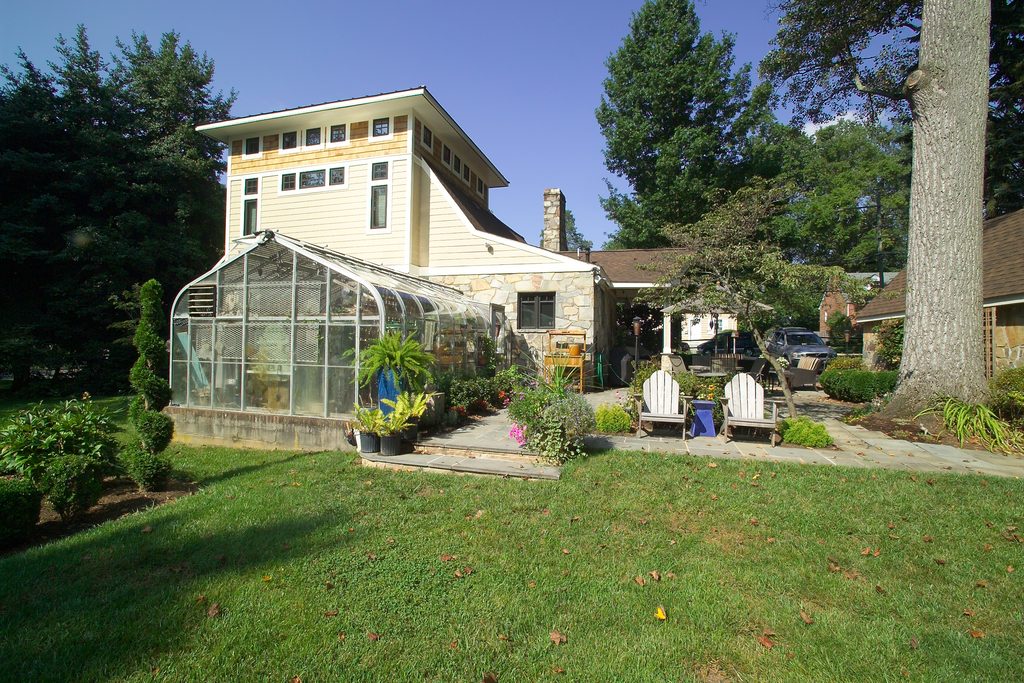 Backyard view of a home addition behind a preserved greenhouse and garden