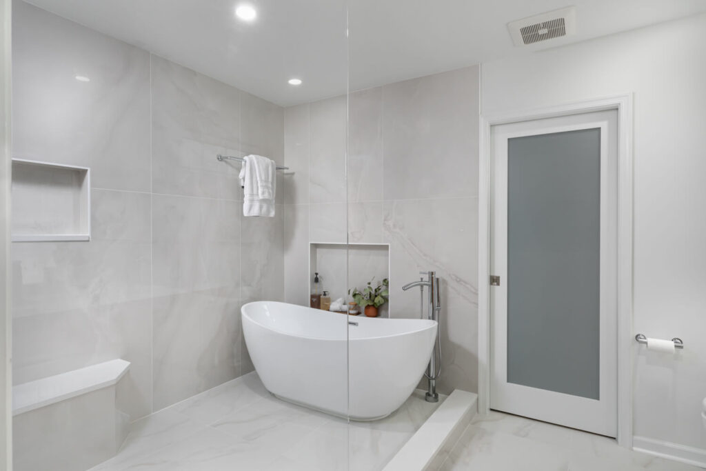 Serene wet room primary bathroom in Falls Church, Virginia with freestanding soaking tub, natural elm floating vanity, and marble-look porcelain tile