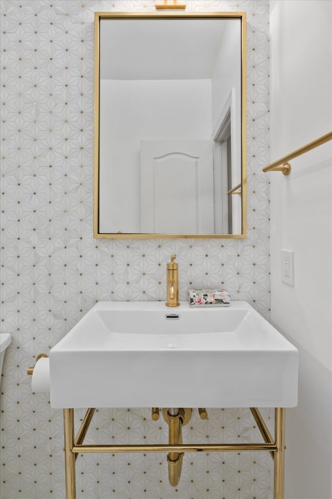 Gold bathroom vanity with a champagne bronze faucet in front of a white, gray, and brass porcelain accent wall