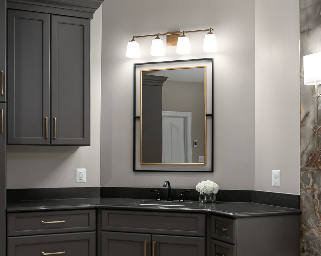Aged brass vanity light above a black and gold framed mirror in a spa bathroom