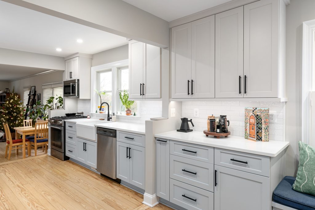 White fireclay farmhouse sink under a pair of windows with a matte black faucet
