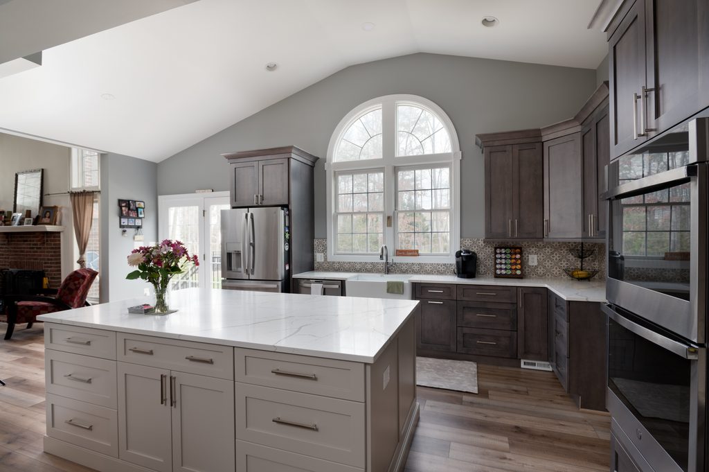 Vaulted kitchen ceiling with an arched Palladian window above a white farmhouse sink and stained maple cabinets