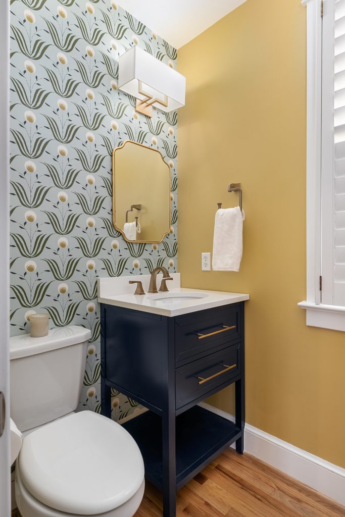 Powder room with floral wallpaper, a navy free-standing vanity, and bronze fixtures